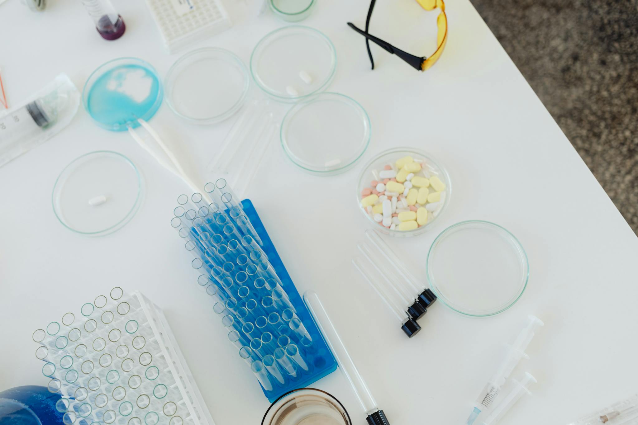 Aerial view of laboratory equipment including petri dishes, pills, test tubes, and syringes.