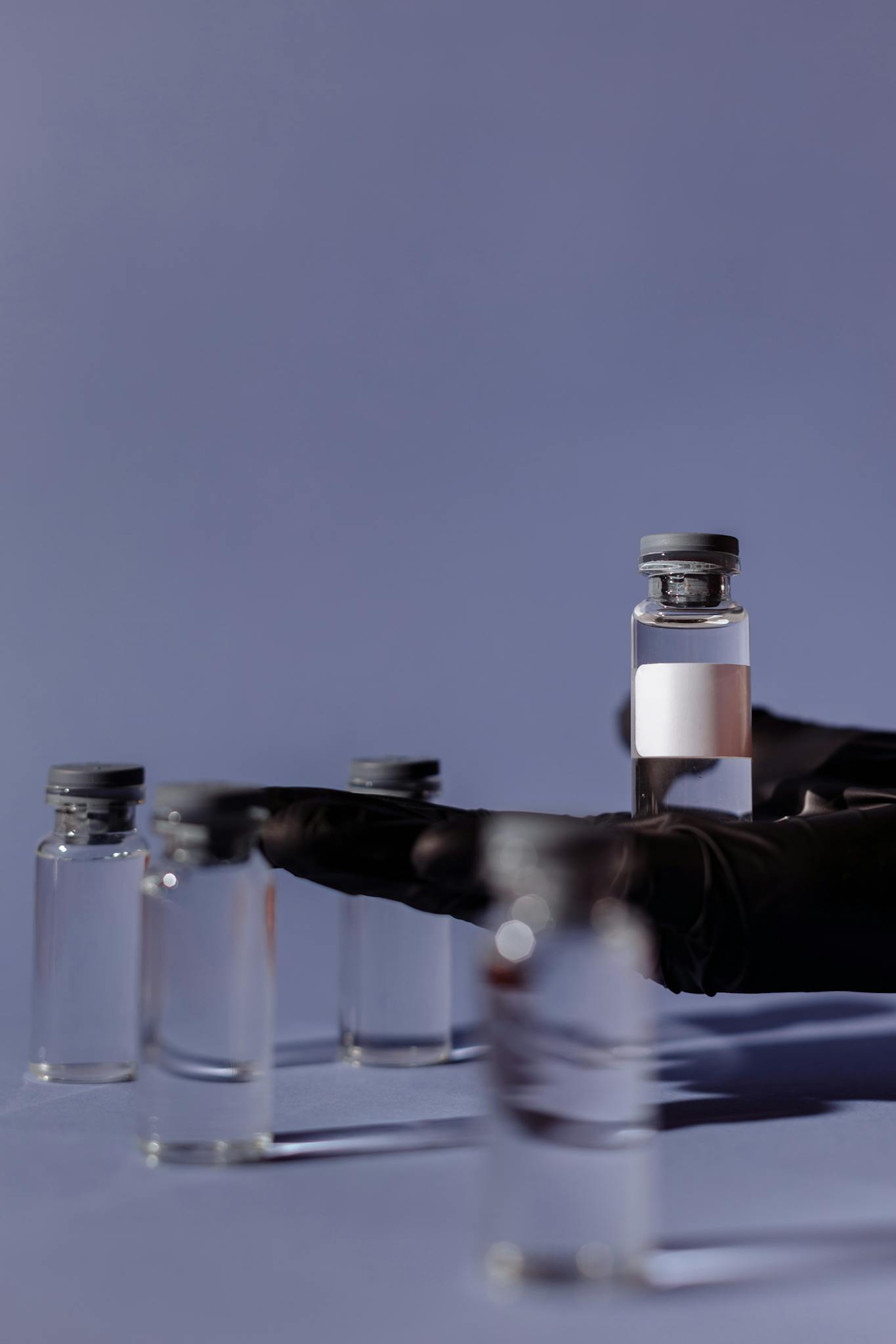 Close-up of vaccination vials with medical gloves holding one, against a soft blue background.